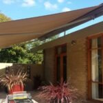 Beige folding arm awning extended over a brick house patio