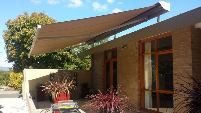 Beige folding arm awning extended over a brick house patio
